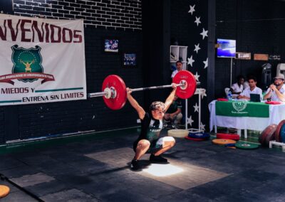 Athlete executing a snatch lift at a weightlifting competition indoors.