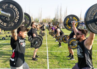 Strong athletes competing in an outdoor weightlifting event, lifting barbells in daylight.
